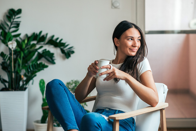 Beautiful young woman drinking tea at home. Looking away.
